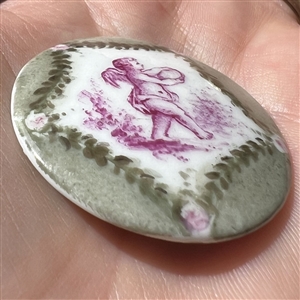 Ceramic button of cherub in purple and green colors.
