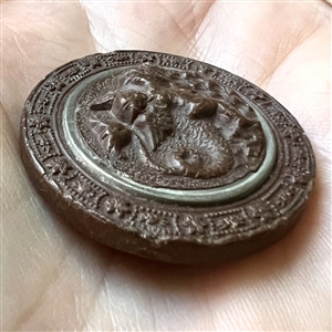 Gutta Percha button of cherub riding a dragon.