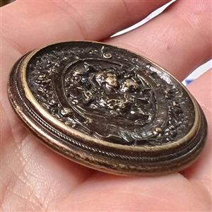Stamped brass button of woman interacting with a cherub.
