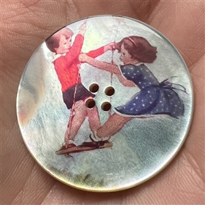 Transfer on iridescent shell button of two children on a swing.
