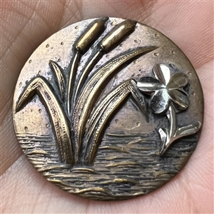 Stamped brass button of cattails and a flower.