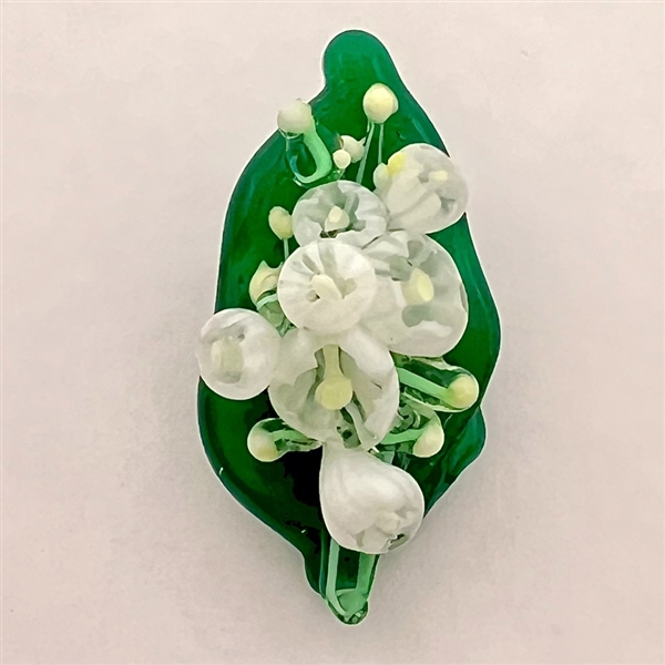 Mary Gaumond’s white "lily of valley" flowers on a leaf studio button.