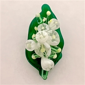 Mary Gaumond’s white "lily of valley" flowers on a leaf studio button.
