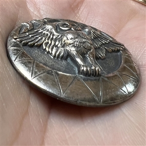 Silvered brass button of an owl over a crescent moon with clouds.