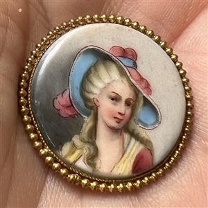 Porcelain button of women in blue and pink hat.