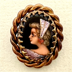 Oval enamel button with foil of a woman’s profile.