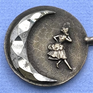 A button closure of brass with a woman and a jester and steel moons.