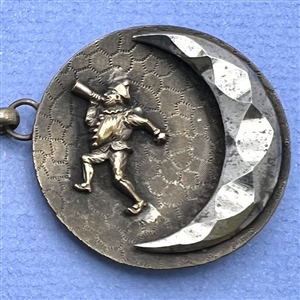 A button closure of brass with a woman and a jester and steel moons.