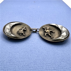 A button closure of brass with a woman and a jester and steel moons.