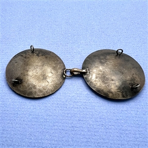 A button closure of brass with a woman and a jester and steel moons.