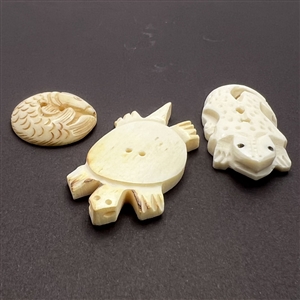 Three carved natural material buttons of animals.