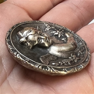 Silvered brass button of a cherub with flowers.
