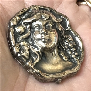 White metal button of a woman’s head with grapes.