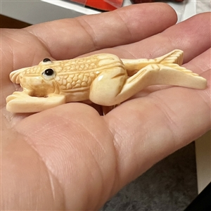 Carved natural material button of a frog.