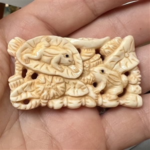 Carved natural material button of frogs and leaves.