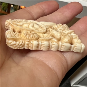 Carved natural material button of frogs and leaves.