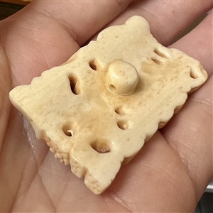 Carved natural material button of frogs and leaves.