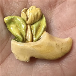 Painted plaster button of a clog holding a tulip.