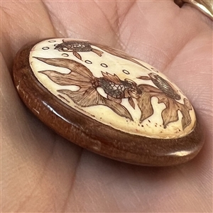 Carved material in wood button of a three koi swimming.