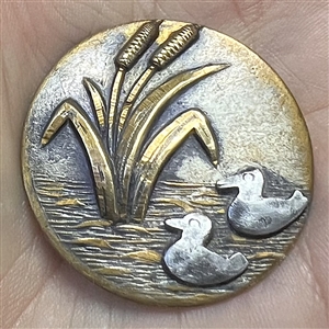 Brass button of cattails and cut steel ducks.