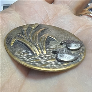 Brass button of cattails and cut steel ducks.