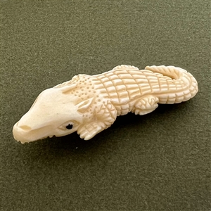 Carved natural material button of an alligator.
