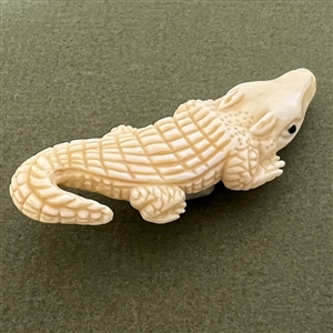Carved natural material button of an alligator.