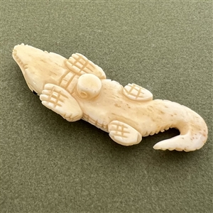 Carved natural material button of an alligator.