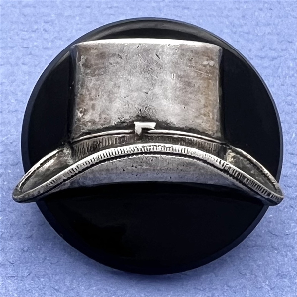 Vintage casein button with silvered metal escutcheon of a top hat.