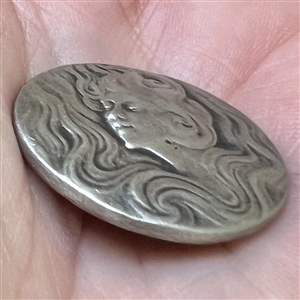 Art Nouveau style Battersea pewter button of a woman with flowing hair.