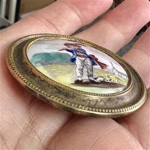 Painted porcelain button of a boy in blue playing a flute.