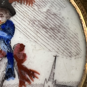 Painted porcelain button of a boy in blue playing a flute.