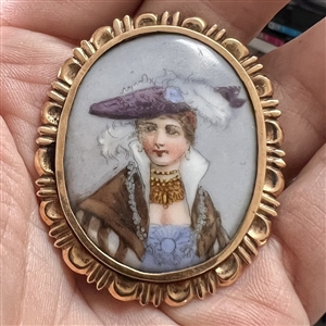 Painted porcelain button of a woman in feathered hat and shawl.