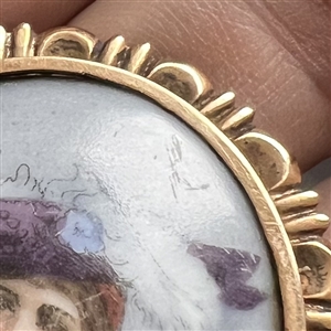 Painted porcelain button of a woman in feathered hat and shawl.