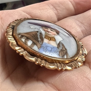 Painted porcelain button of a woman in feathered hat and shawl.