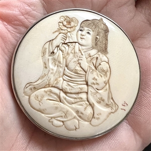 Incised, inked or painted natural material button of an Asian girl with a flower.