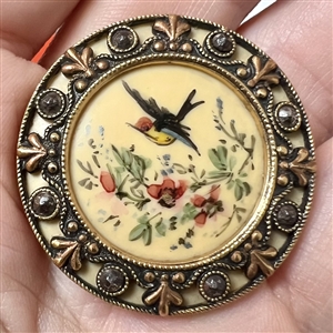 A Victorian painted bird in flight on celluloid set in metal with cut steels button.