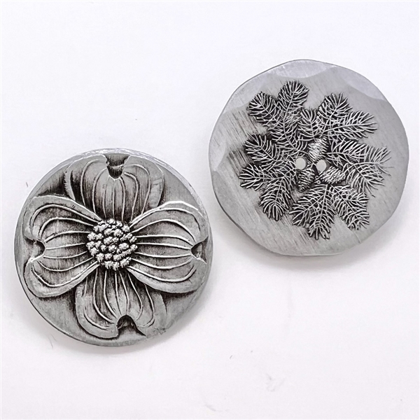 Two aluminum buttons of a dogwood flower and pinecone from Wendell August Forge.