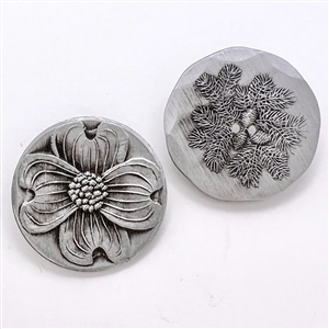 Two aluminum buttons of a dogwood flower and pinecone from Wendell August Forge.