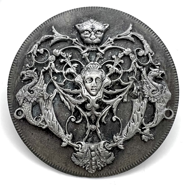 Pewter escutcheon over white metal button of a face and mythological creatures.