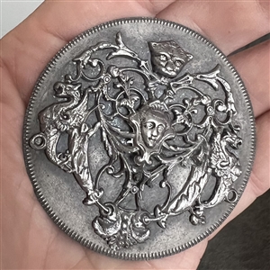 Pewter escutcheon over white metal button of a face and mythological creatures.