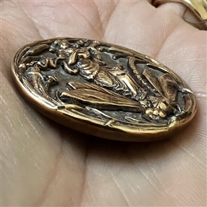 Brass button of a sprite (?) riding a dragonfly while playing an instrument.