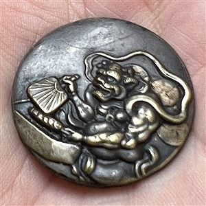 Japanese metal work button of a masked character with a fan. 