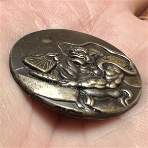 Japanese metal work button of a masked character with a fan. 