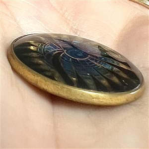 Fern-like design reverse painted on glass over gold and blue lusters set in metal button.