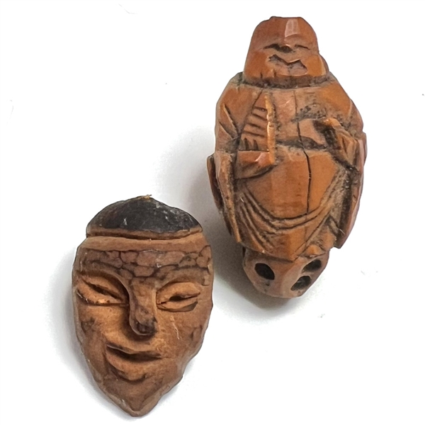 Two Folk Art carved fruit pit buttons of people.