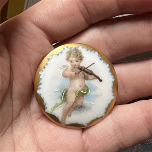 Painted porcelain button of a cherub playing a violin. 