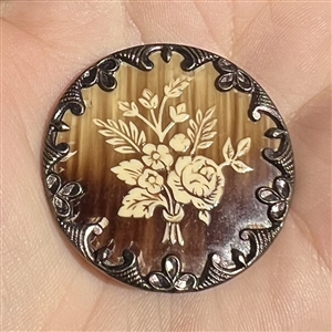 Victorian celluloid button set in metal with floral design.