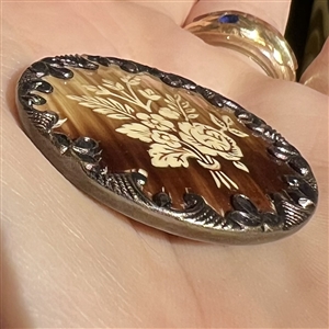 Victorian celluloid button set in metal with floral design.