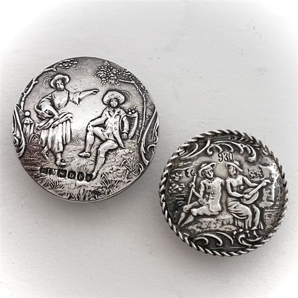 Two silver buttons of people in nature.